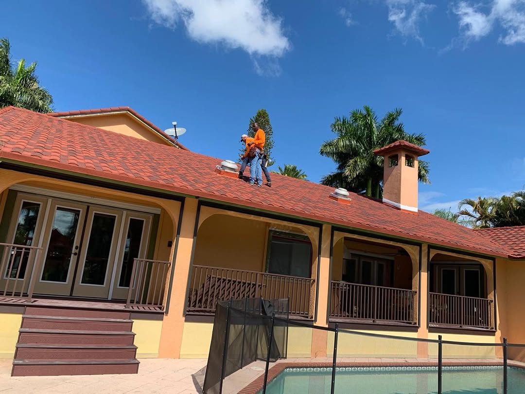Two roofers in orange shirts on red tile roof