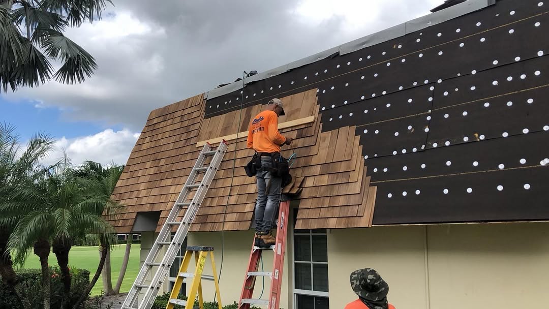Roofer installing cedar shake shingles on ladder